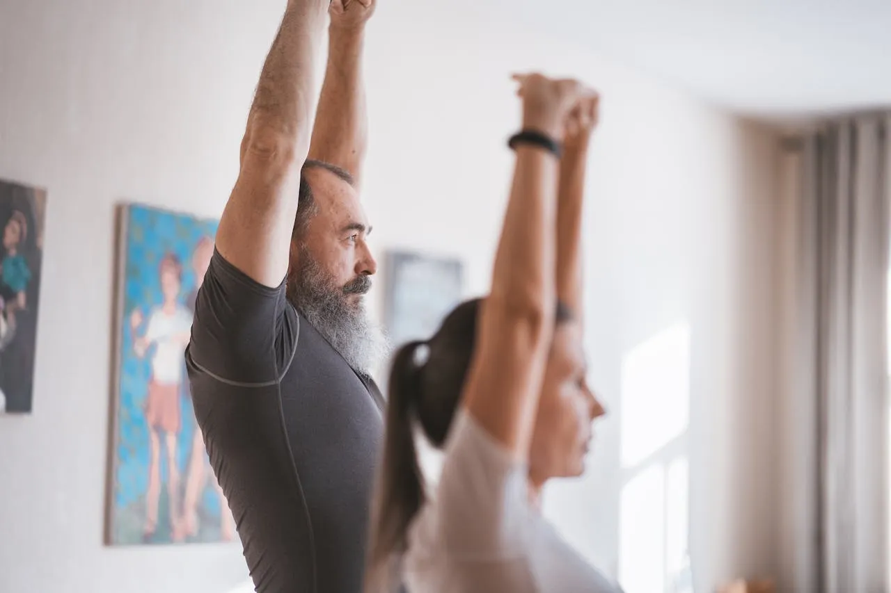 Older man and a woman stretching their arms overhead together during an indoor exercise class