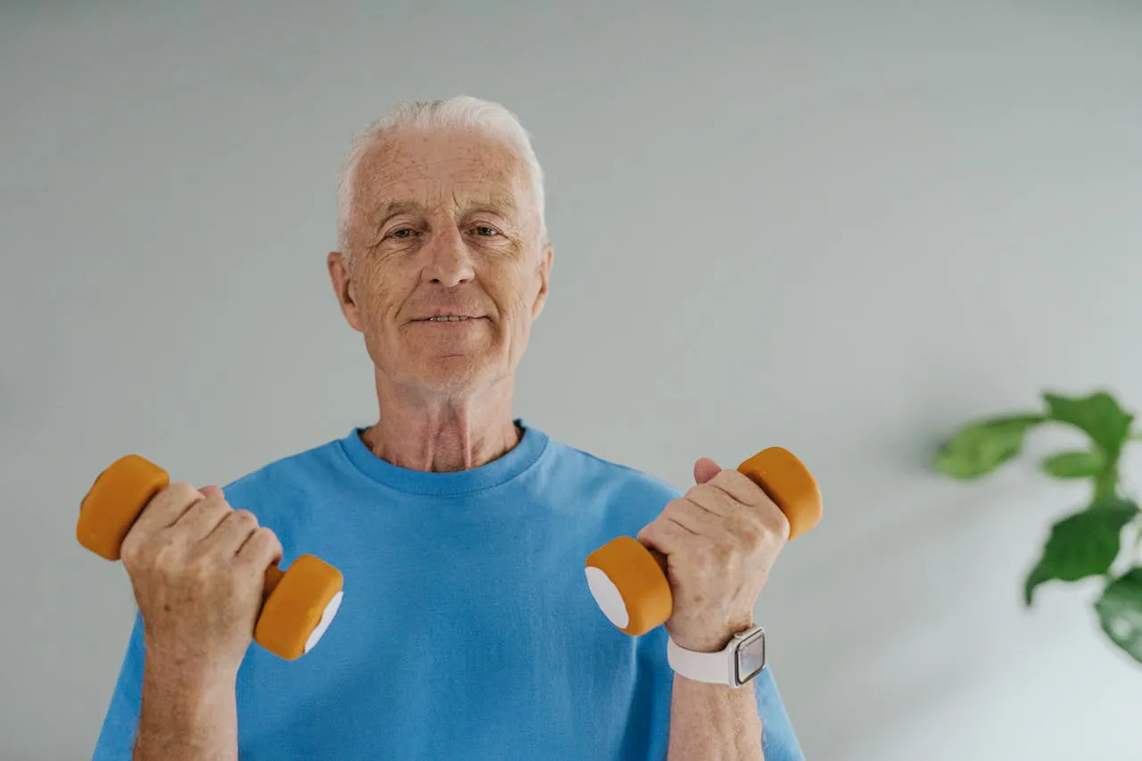 Smiling older man in a blue t-shirt lifting a pair of light hand weights